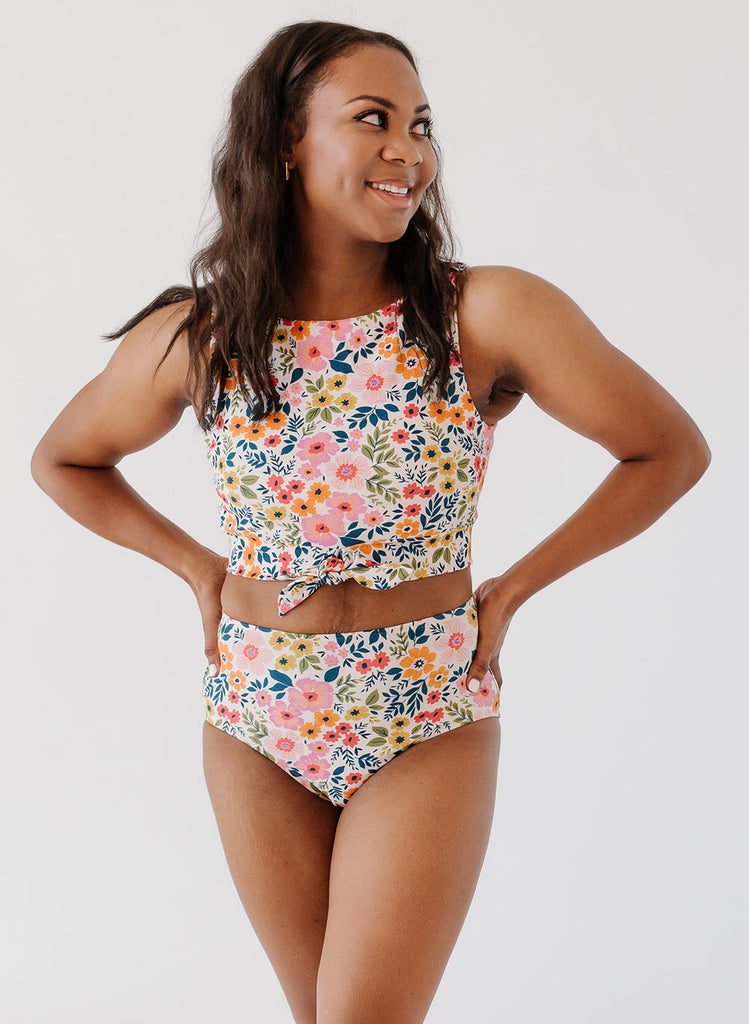 Photo of woman with her hands on her hips wearing a multi colored floral cropped swim top with multi colored floral high waist swim bottoms