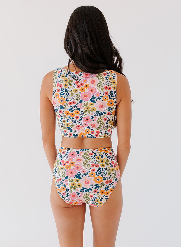 Photo of woman with her back facing us wearing a multi colored floral cropped swim top multi colored floral high waist swim bottoms