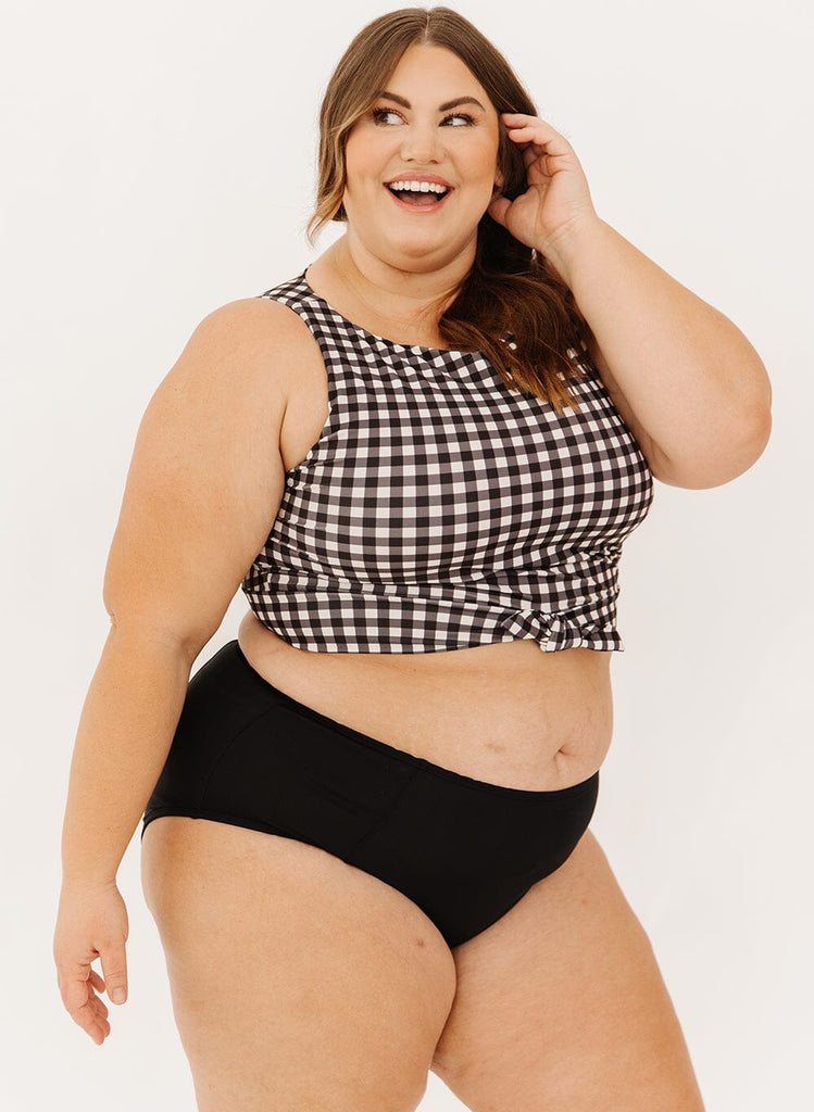 Photo of a woman wearing black high-waist swim bottoms with a black gingham knotted crop swim top