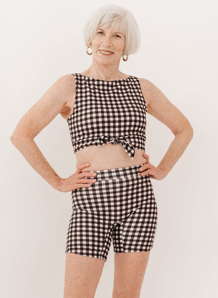 Photo of a woman wearing black gingham bike swim shorts and a black gingham knotted swim crop top