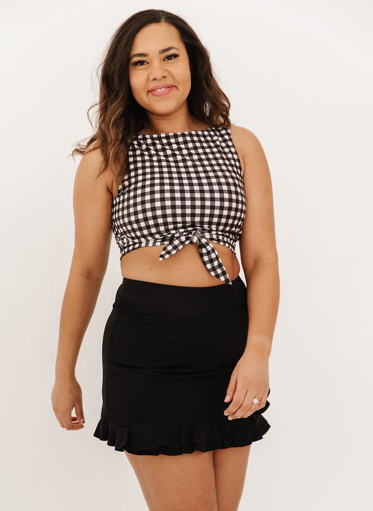 Photo of a woman wearing a black high-waist ruffle swim skirt with a black gingham knotted swim crop top
