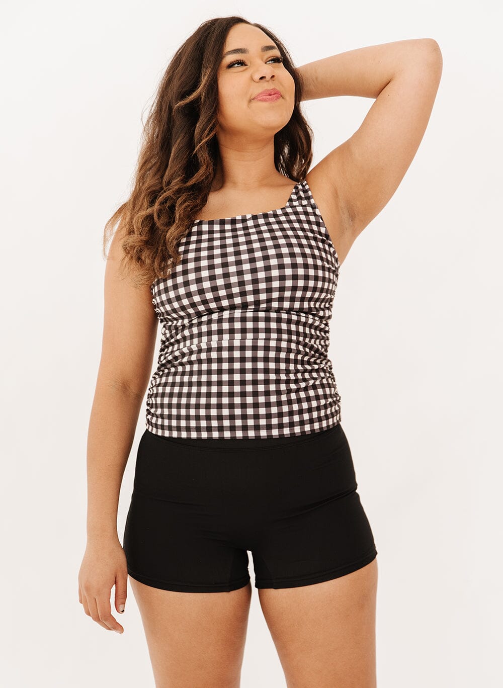 Photo of a woman wearing high-waist black swim shorts and a black gingham square neck tankini swim top