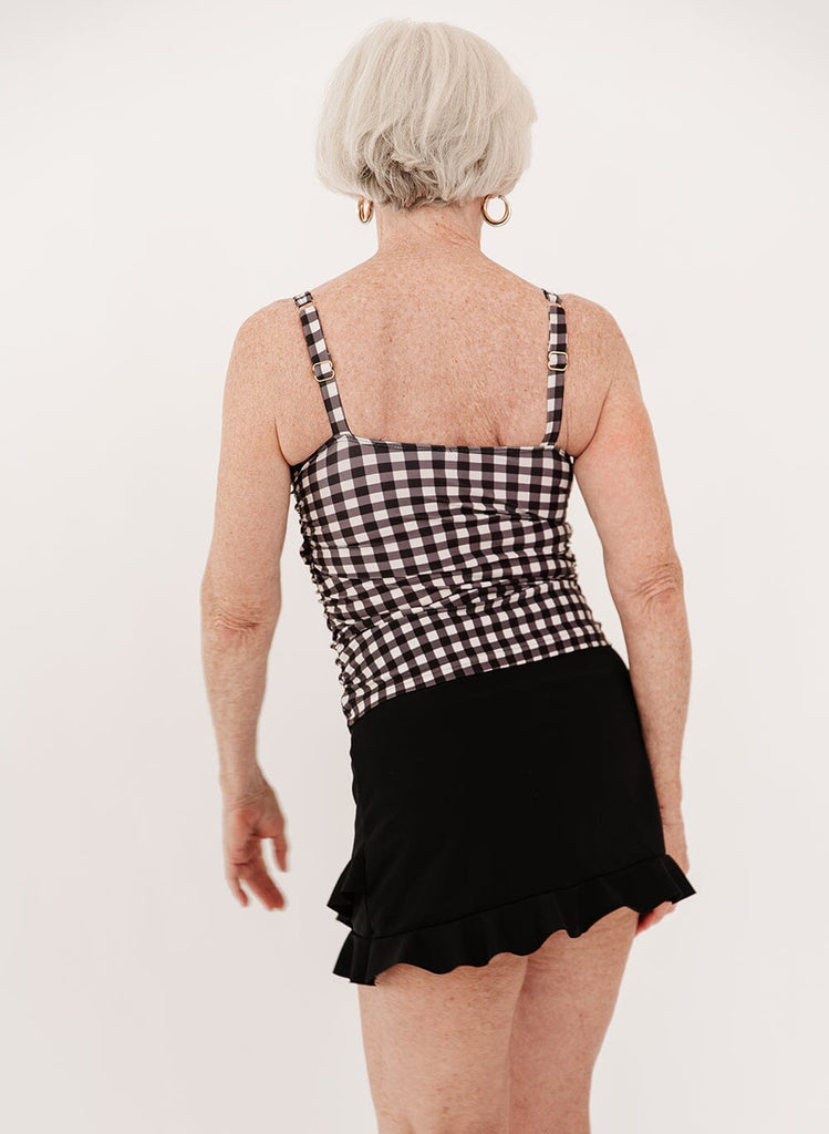 Photo of a woman wearing a black high-waist ruffle swim skirt with a black gingham square neck tankini swim top