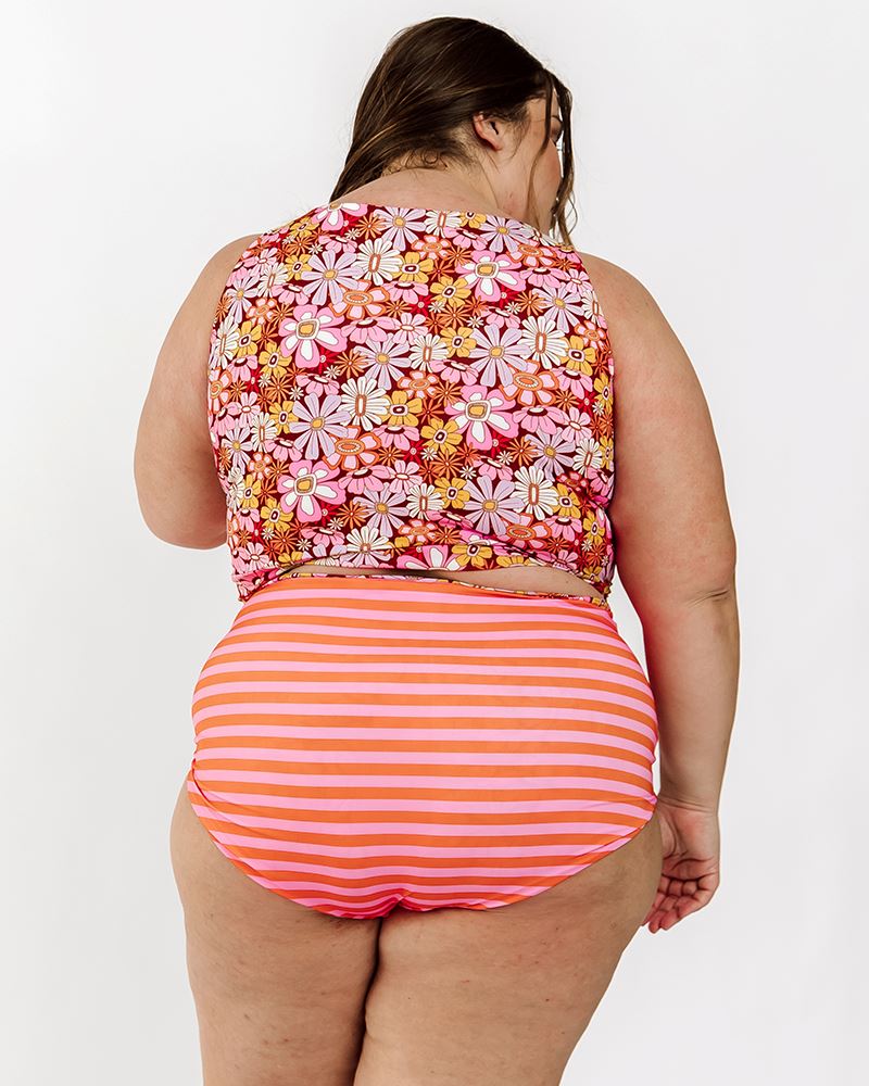 Photo of a woman wearing a Groovy Blooms/sherbet stripe reversible swim bottom stripe side and s groovy Blooms floral swim crop top back angle