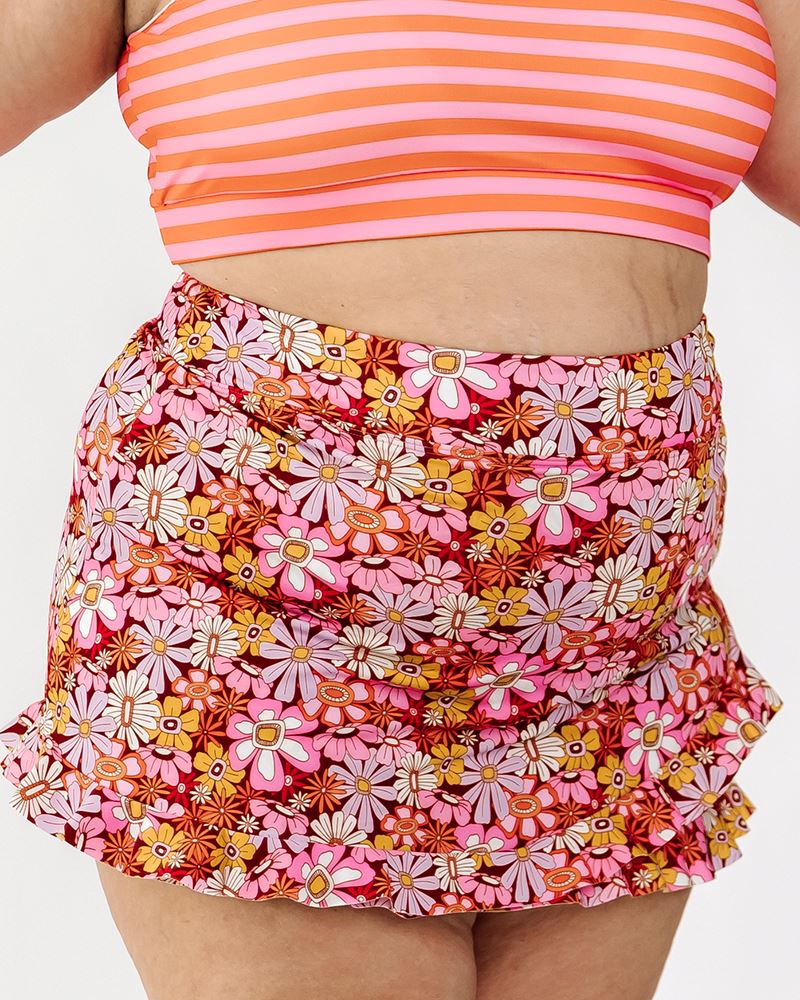 Photo of a woman wearing a groovy Blooms floral swim skirt bottom and an orange and pink stripe swim bralette