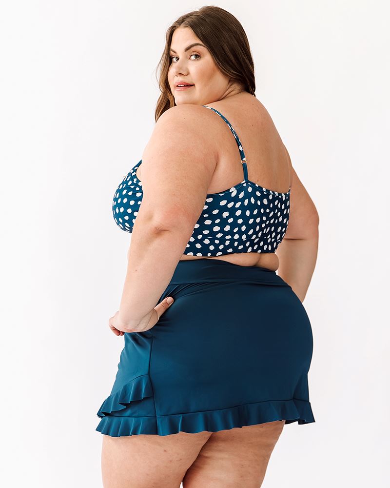 Photo of a woman wearing an Indigo dot swim bralette and an Indigo swim skirt bottom side/back angle