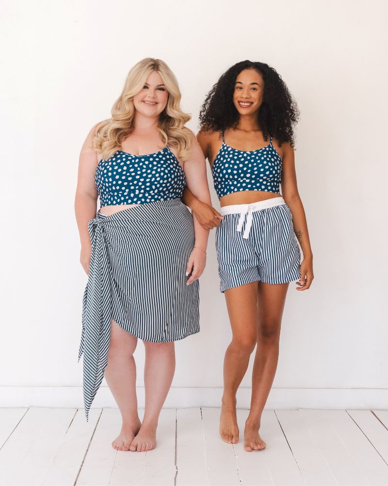 Photo of two women wearing blue and white stripe swim board shorts and a blue and white dotted swim bralette and a blue and white stripe sarong