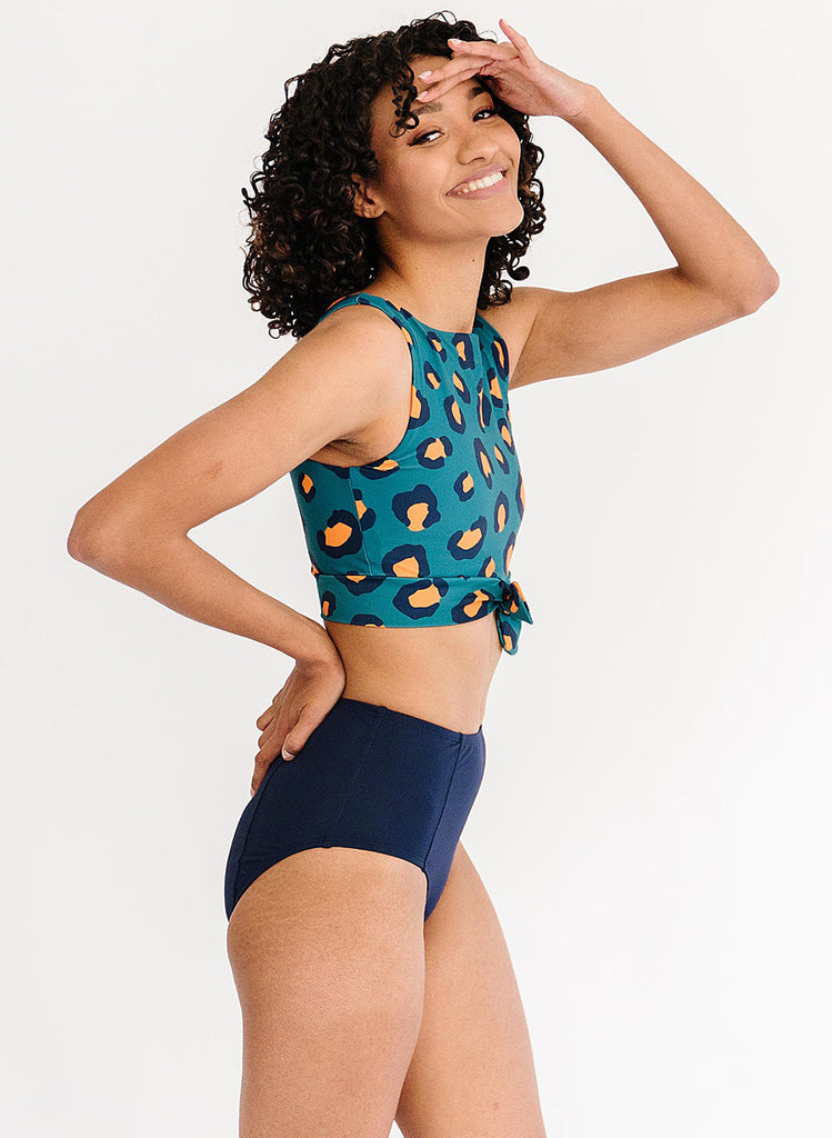 Photo of a woman with her hand on her head wearing a blue leopard print cropped swim top with blue high waist swim bottoms
