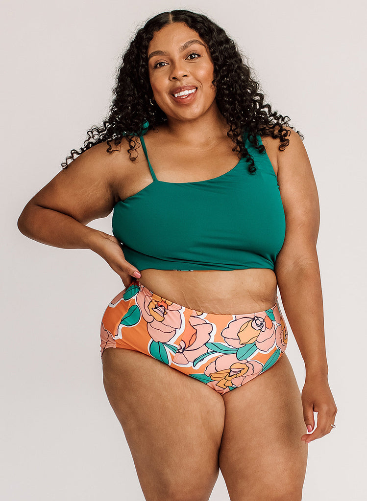 Photo of a woman with her hand on her hip wearing a blue cropped swim top with orange floral high waist swim bottoms