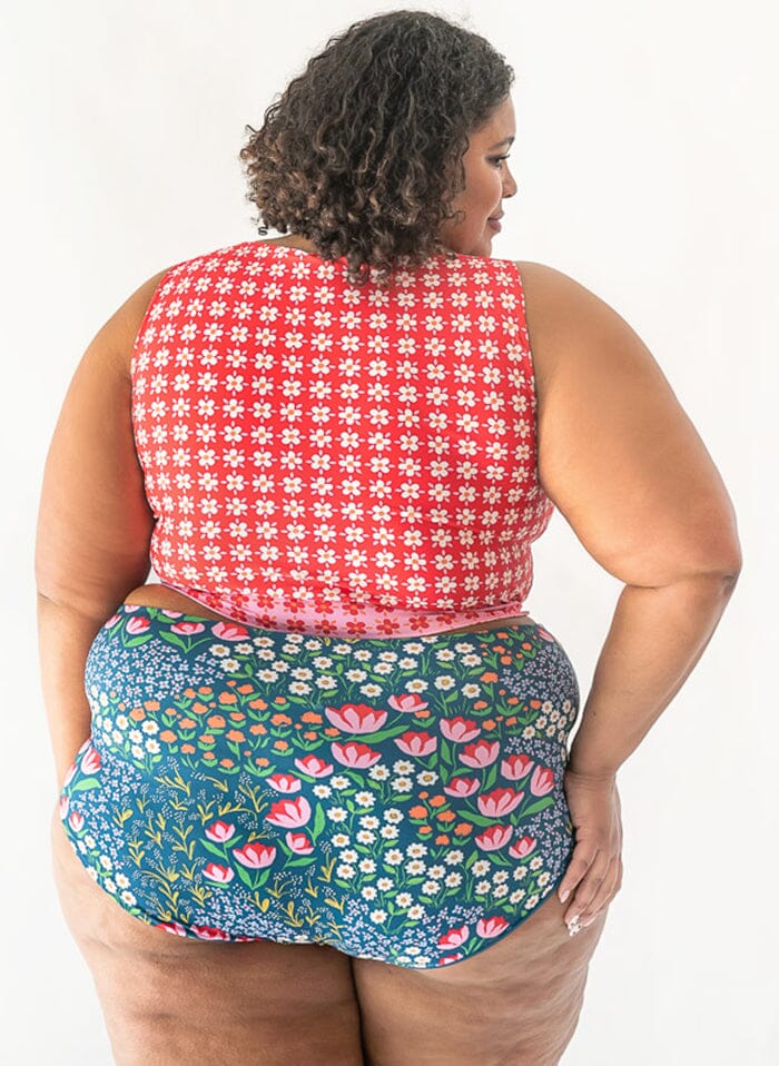 Photo of a woman with her back facing us wearing a red floral cropped swim top with blue floral high waist swim bottoms