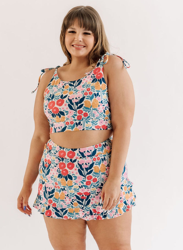 Photo of a woman wearing a may Flowers shoulder-tie swim crop top and a May Flowers swim skirt bottom