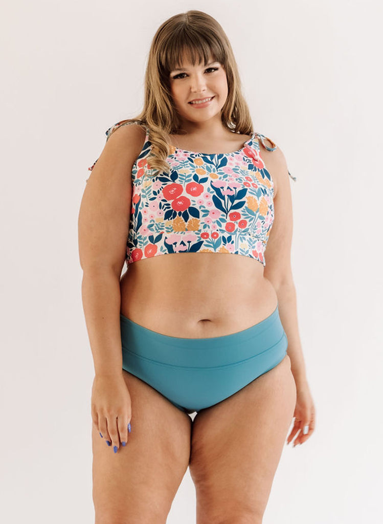 Photo of a woman wearing a may Flowers shoulder-tie swim crop top and an ocean blue swim bottom