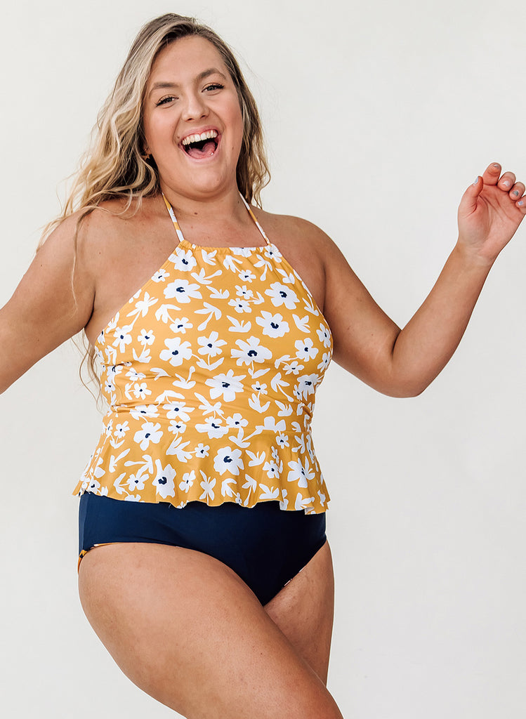 Photo of a woman smiling while wearing a yellow floral swim top with blue high waist swim bottoms