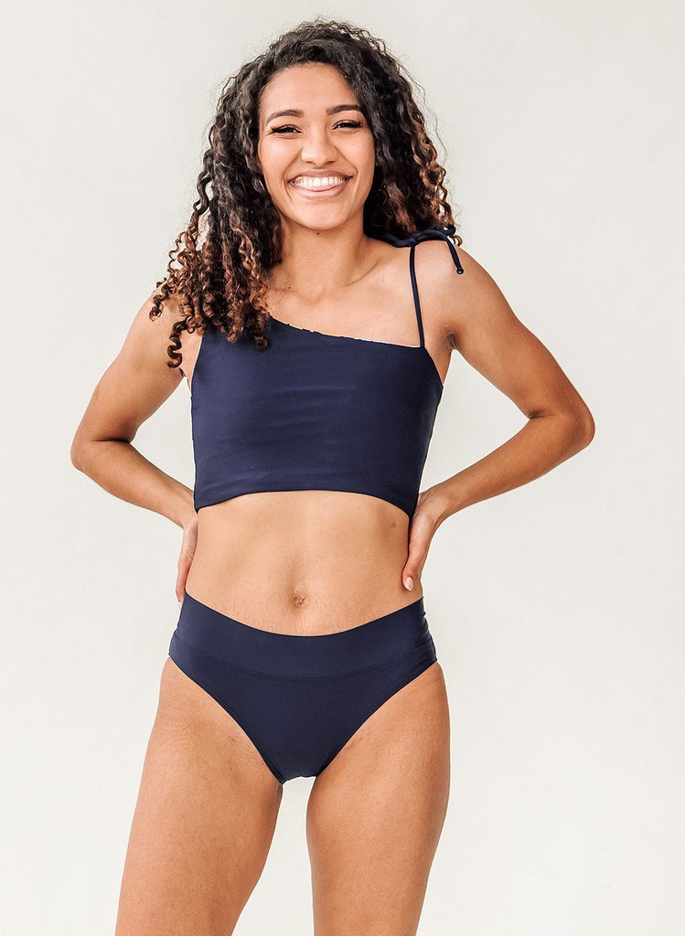 Photo of a woman with her hands on her hips wearing a blue cropped swim top with blue classic low rise swim bottoms