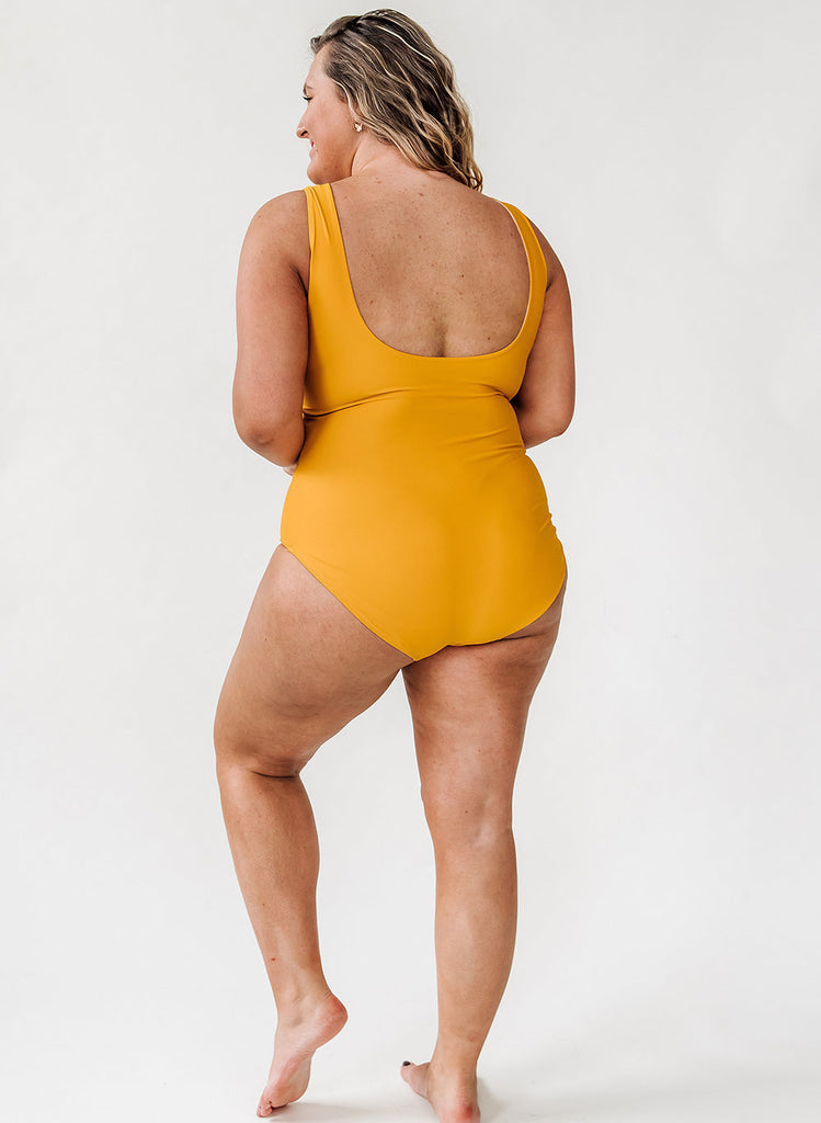 Photo of a woman wearing a mustard yellow one piece swim suit- back angle