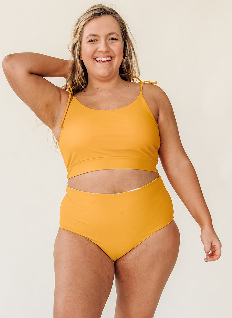 Photo of woman wearing a yellow cropped swim top with yellow high waist swim bottoms