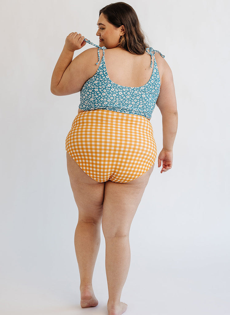 Photo of woman wearing blue floral cropped swim top with yellow and white gingham swim bottoms back angle