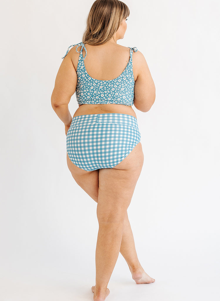 Photo of woman wearing blue floral cropped swim top with blue and white gingham swim bottoms back angle