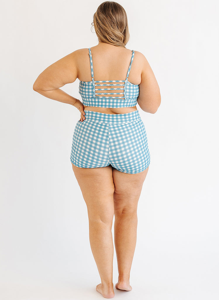 Photo of woman wearing blue and white gingham bralette swim top with blue and white gingham swim shorts back angle