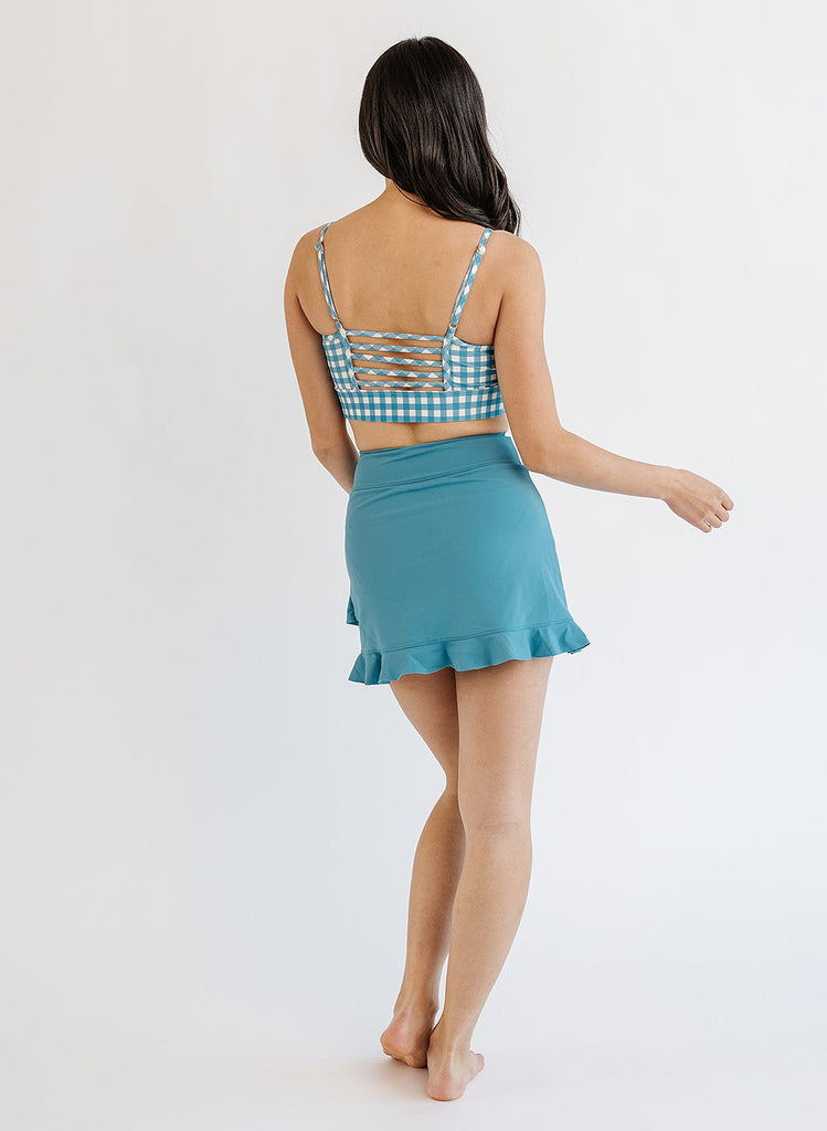 Photo of woman wearing blue and white gingham bralette swim top with blue swim skirt back angle