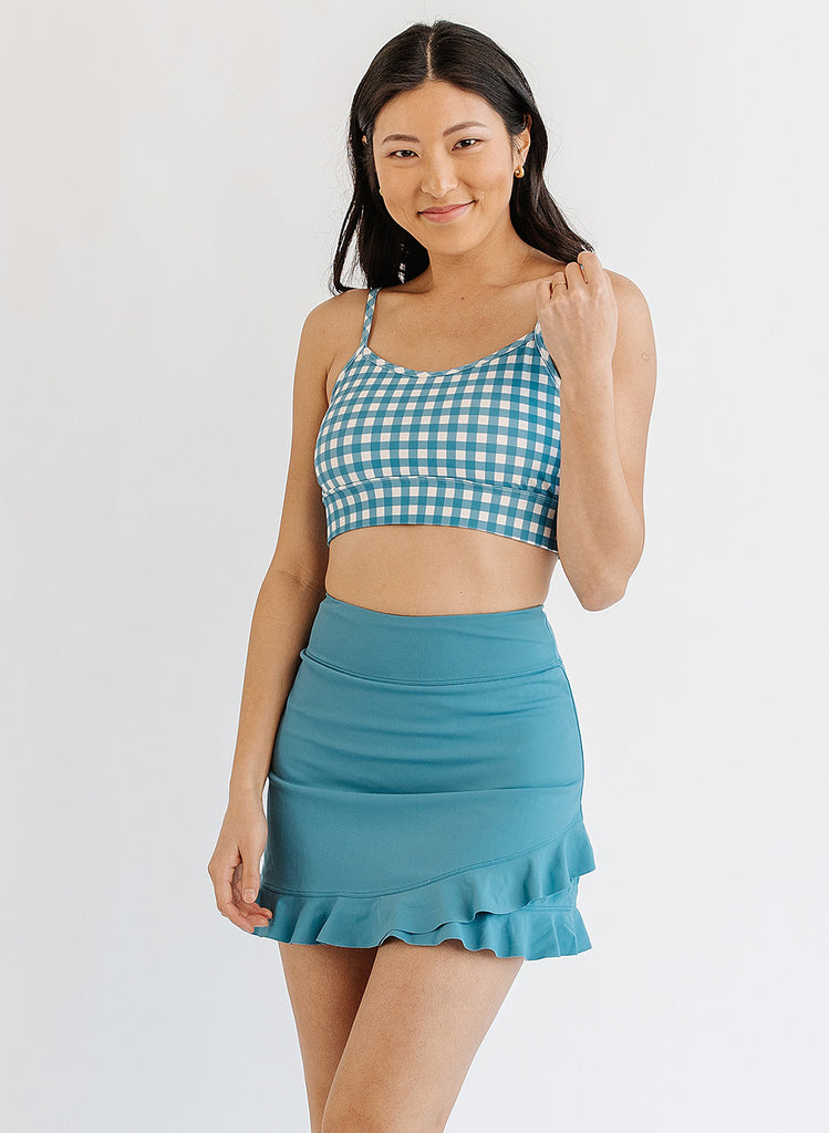 Photo of woman wearing blue and white gingham bralette swim top with blue swim skirt