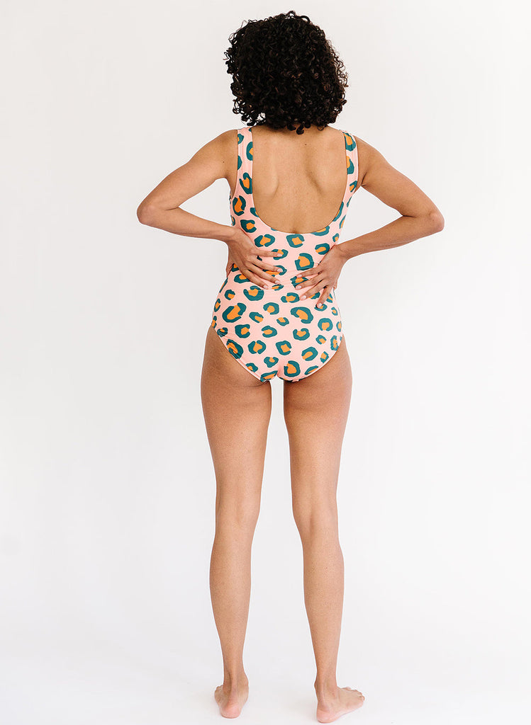 Photo of woman with her back facing us wearing a pink leopard one piece swimsuit