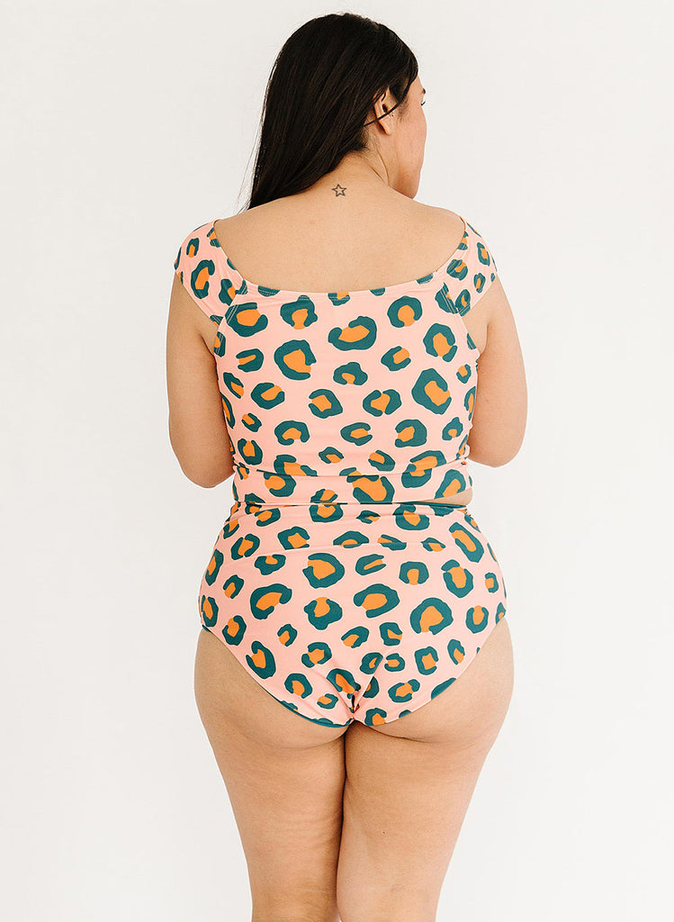Photo of a woman wearing a peach leopard cap-sleeve swim crop top and a peach leopard swim bottom- back angle