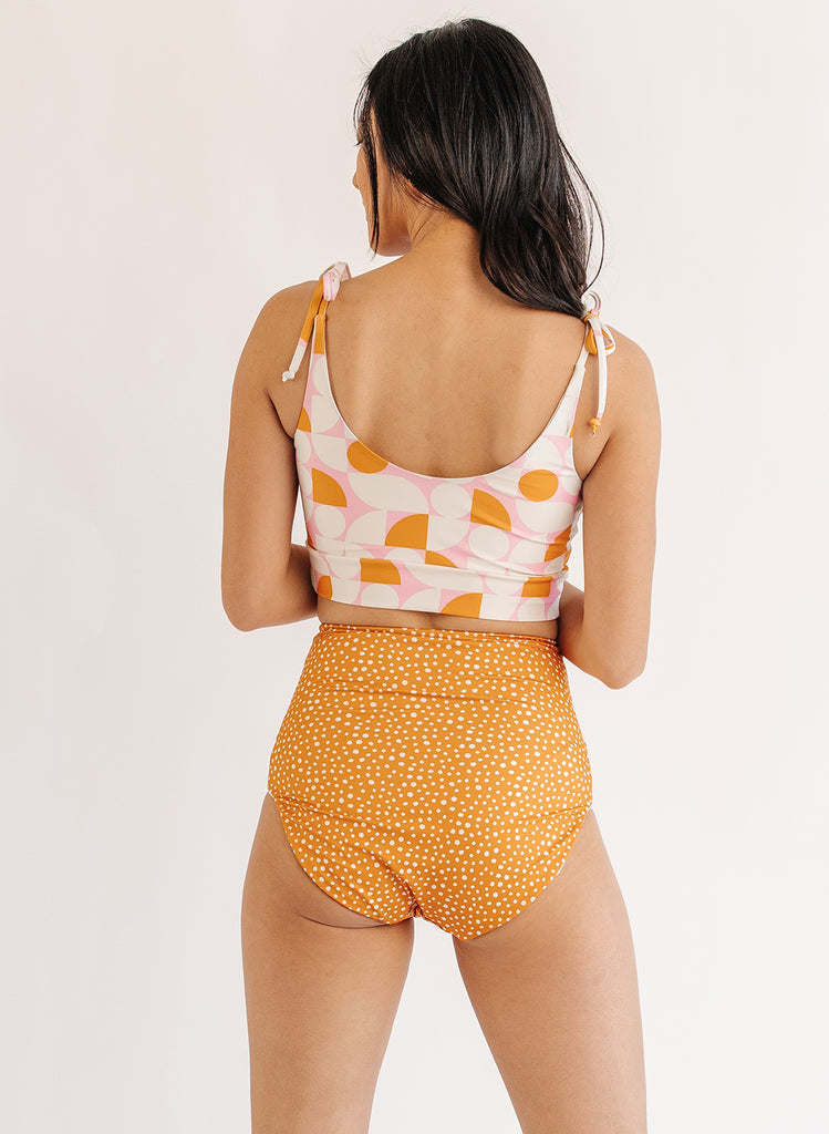 Photo of woman wearing orange and white geometric cropped swim top with orange and white dot swim bottoms back angle