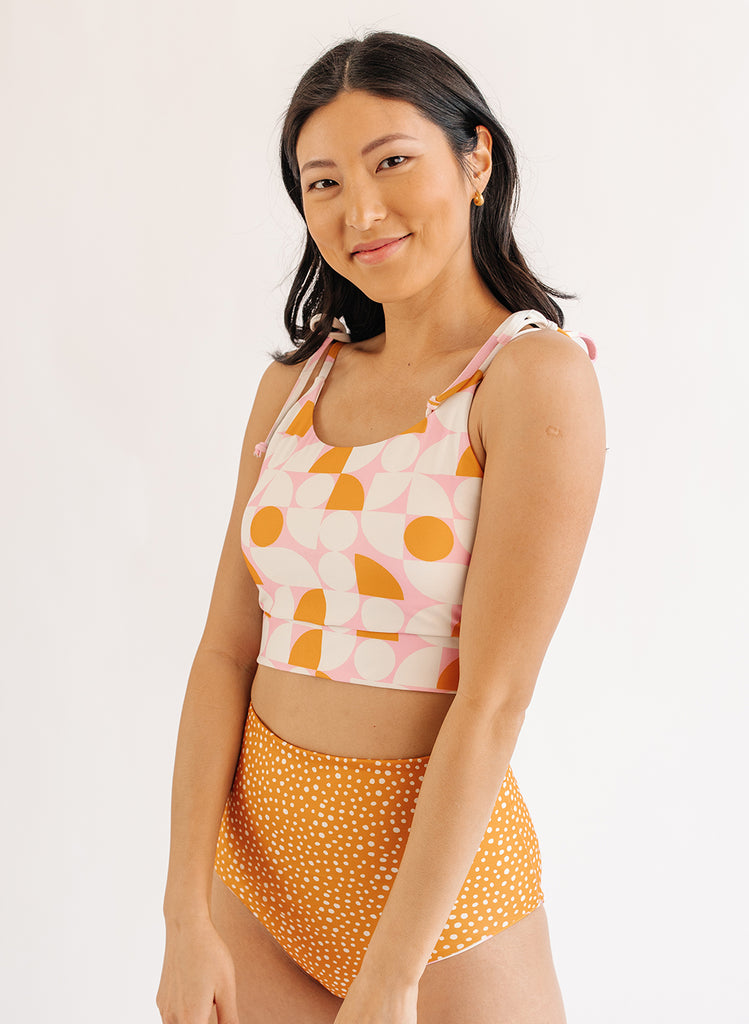 Photo of woman wearing orange and white geometric cropped swim top with orange and white dot swim bottoms