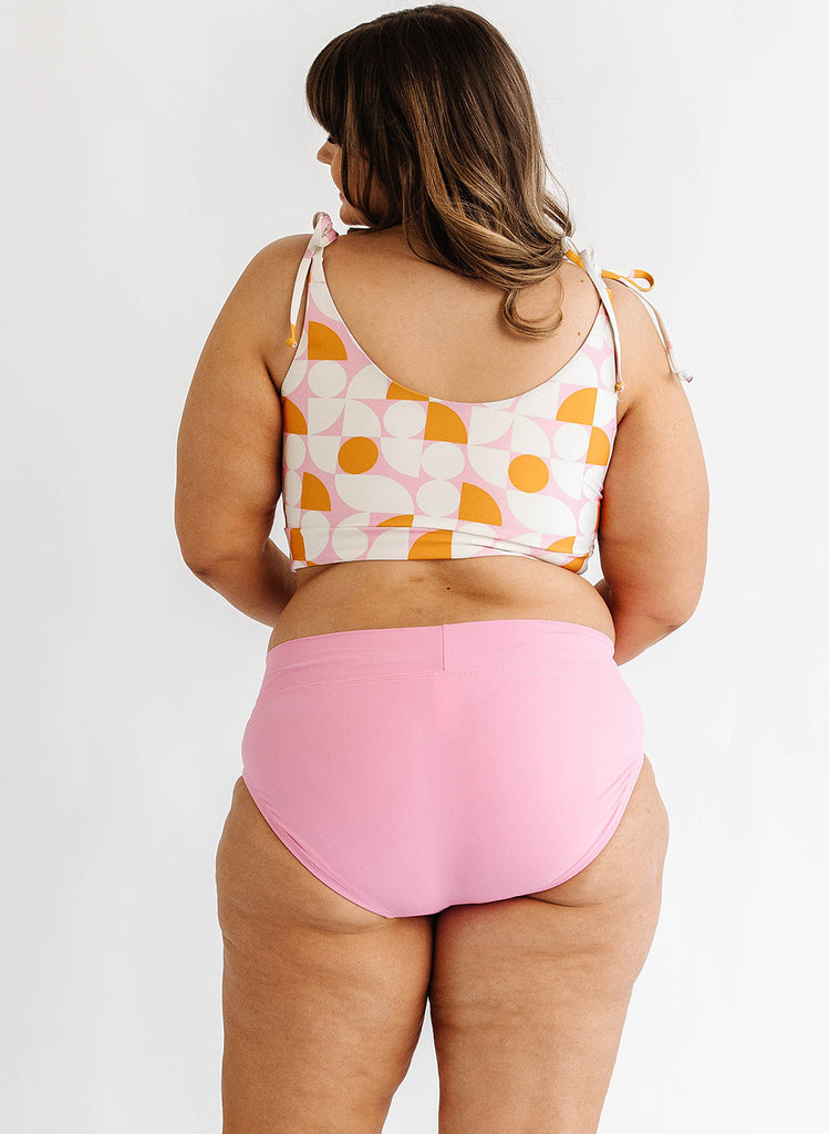 Photo of woman wearing orange and white geometric cropped swim top with pink swim bottoms back angle