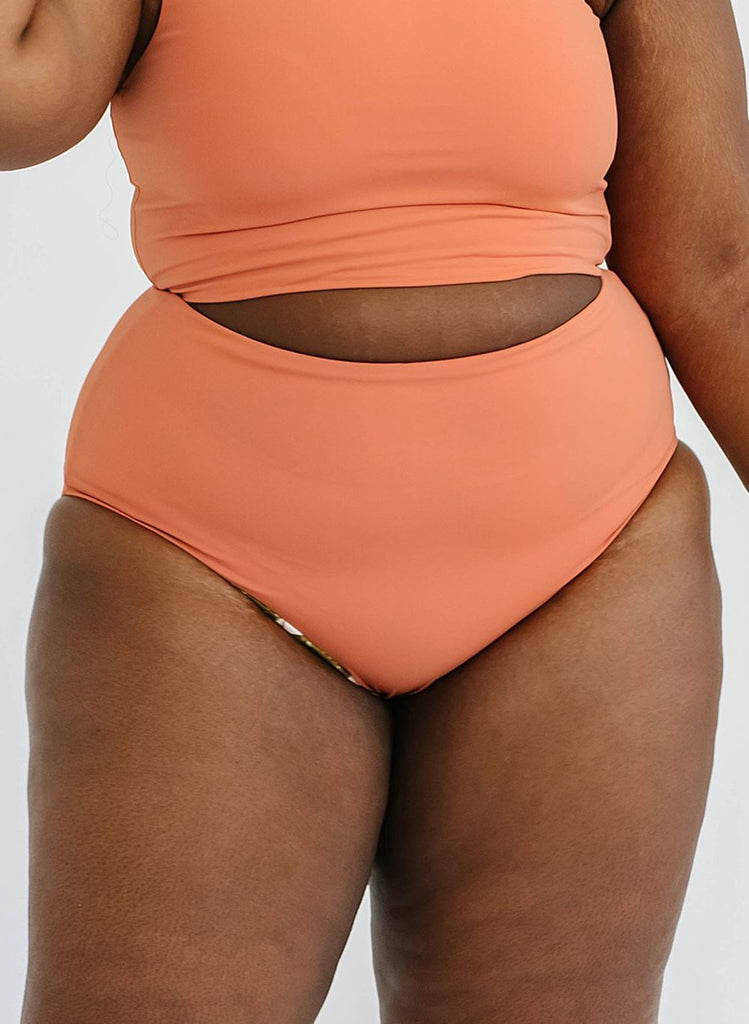 Close up photo of a woman wearing an orange cropped swim top with orange high waist swim bottoms