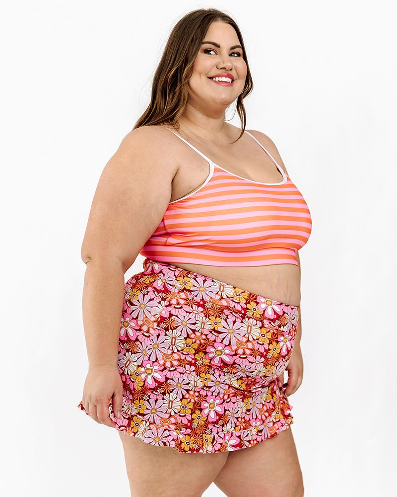 Photo of a woman wearing a Sherbet stripe swim bralette and a groovy Blooms swim skirt bottom side angle