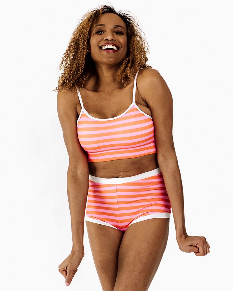 Photo of a woman wearing a Sherbet stripe retro swim short bottom and a sherbet stripe swim bralette