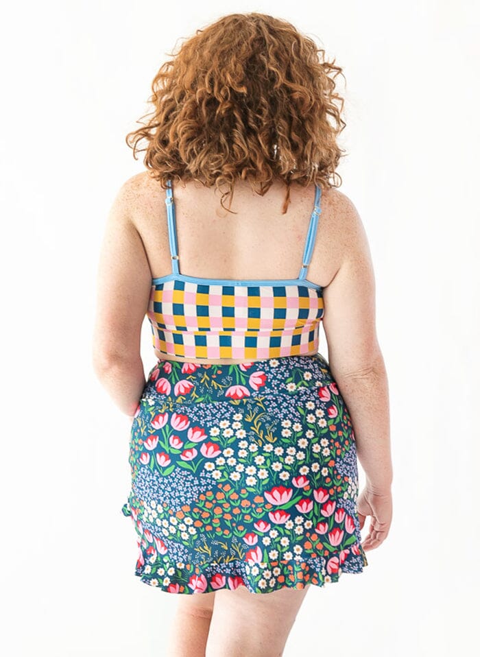 Photo of woman with her back facing us wearing a multi colored checkered cropped swim top with a blue floral swim skirt