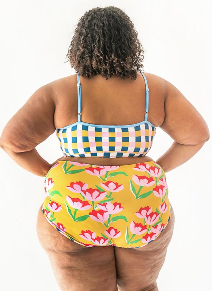 Photo of a woman wearing a multi color checkered swim bralette and a yellow floral swim bottom- back angle