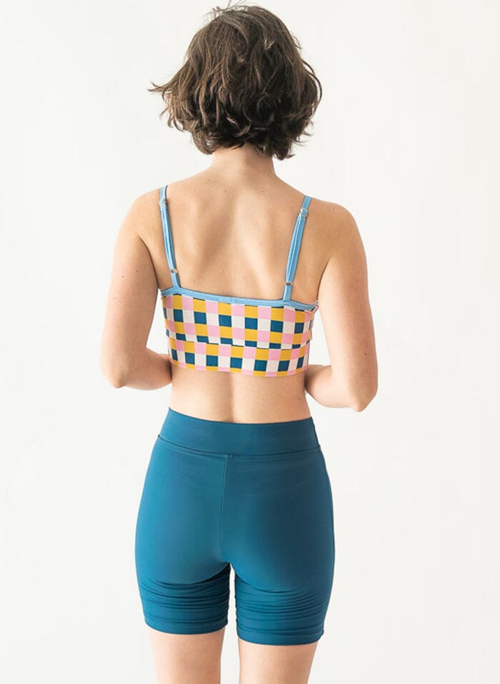 Photo of a woman wearing an indigo swim bike short and a multi-color checkered swim bralette back angle