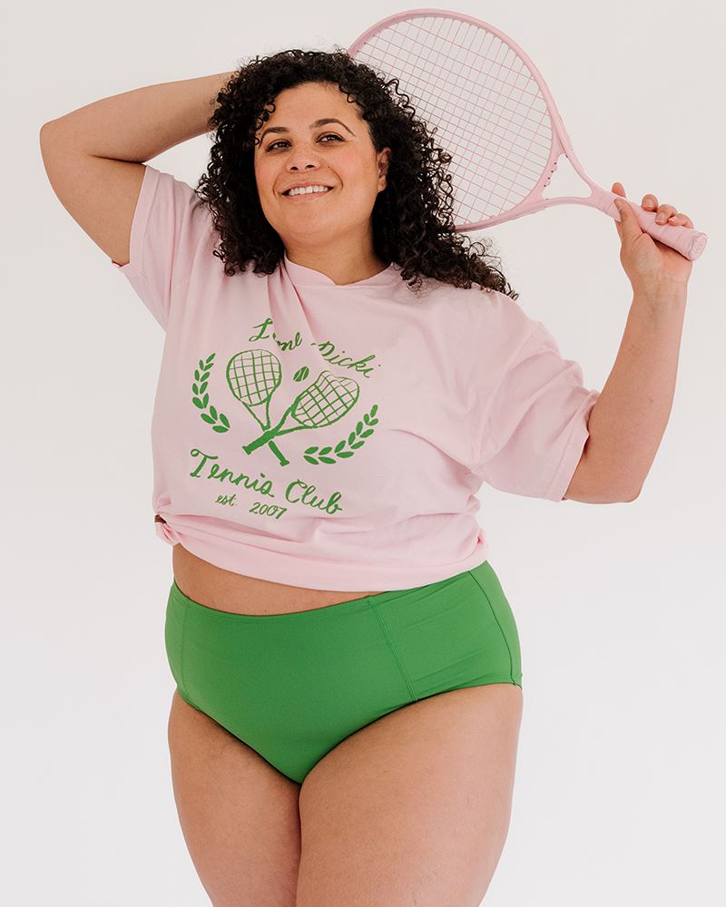 Photo of woman holding tennis racket wearing lime ricki tennis club graphic tee with green swim bottoms