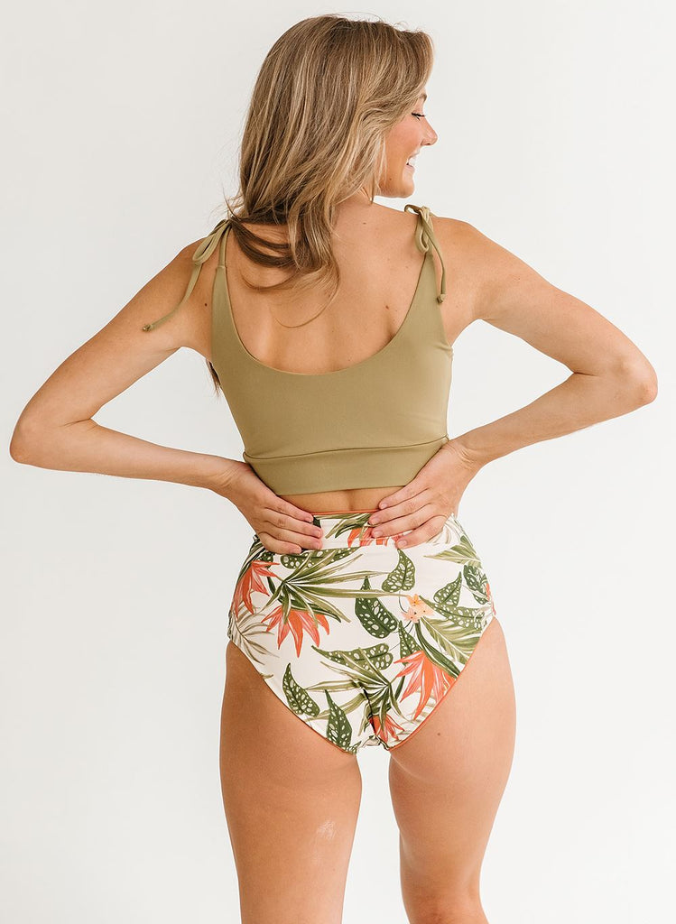Photo of a woman with her back facing us wearing a green cropped swim top with green floral high waist swim bottoms