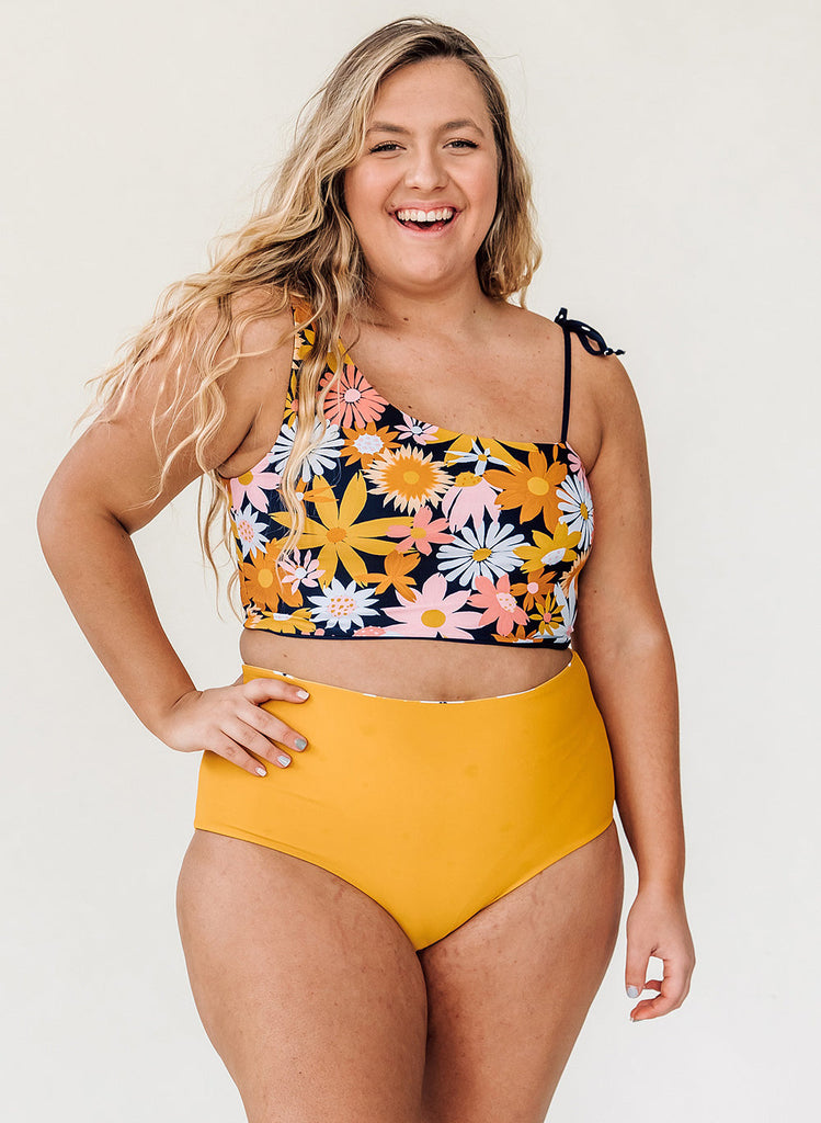 Photo of a woman wearing a multi color one-shoulder floral swim crop top and a mustard yellow swim bottom