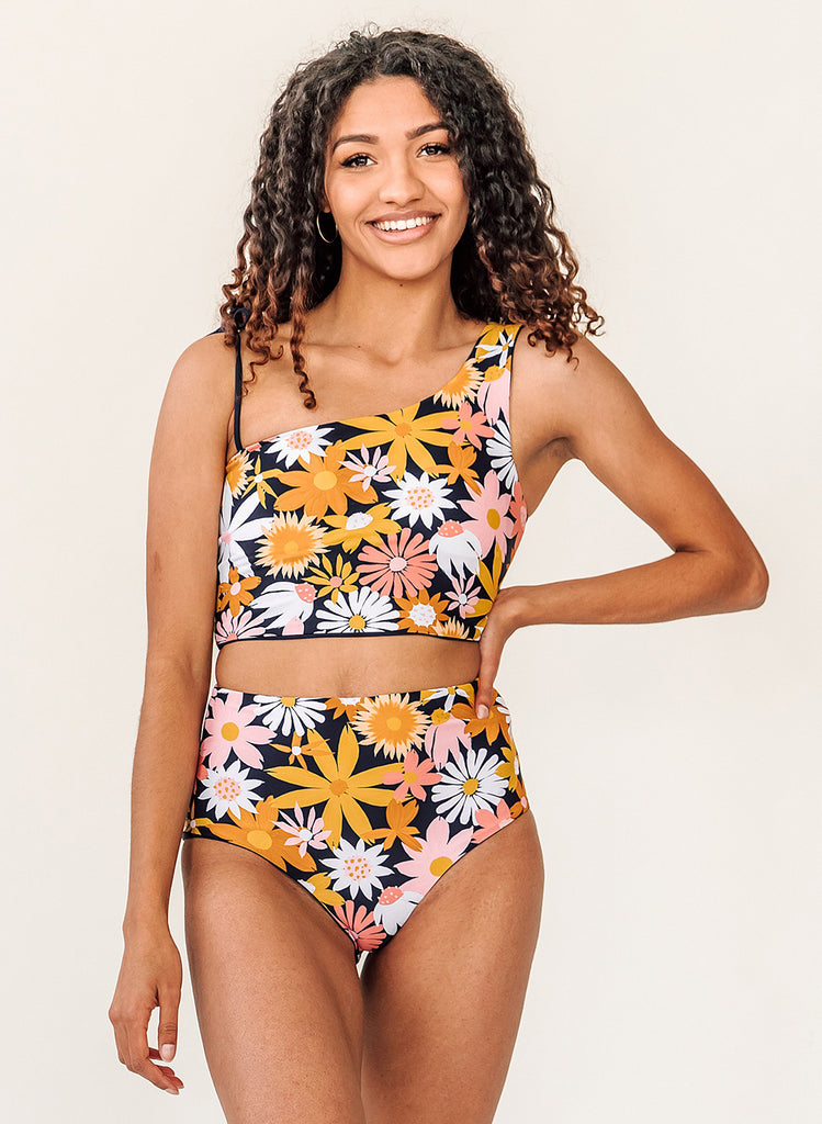Photo of woman with her hand on her hip wearing a yellow and pink floral cropped swim top with yellow and pink high waist swim bottoms