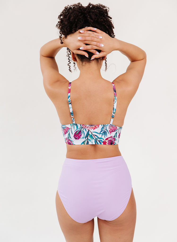 Photo of a woman with her back facing us wearing a blue and white floral cropped swim top with lavender high waist swim bottoms