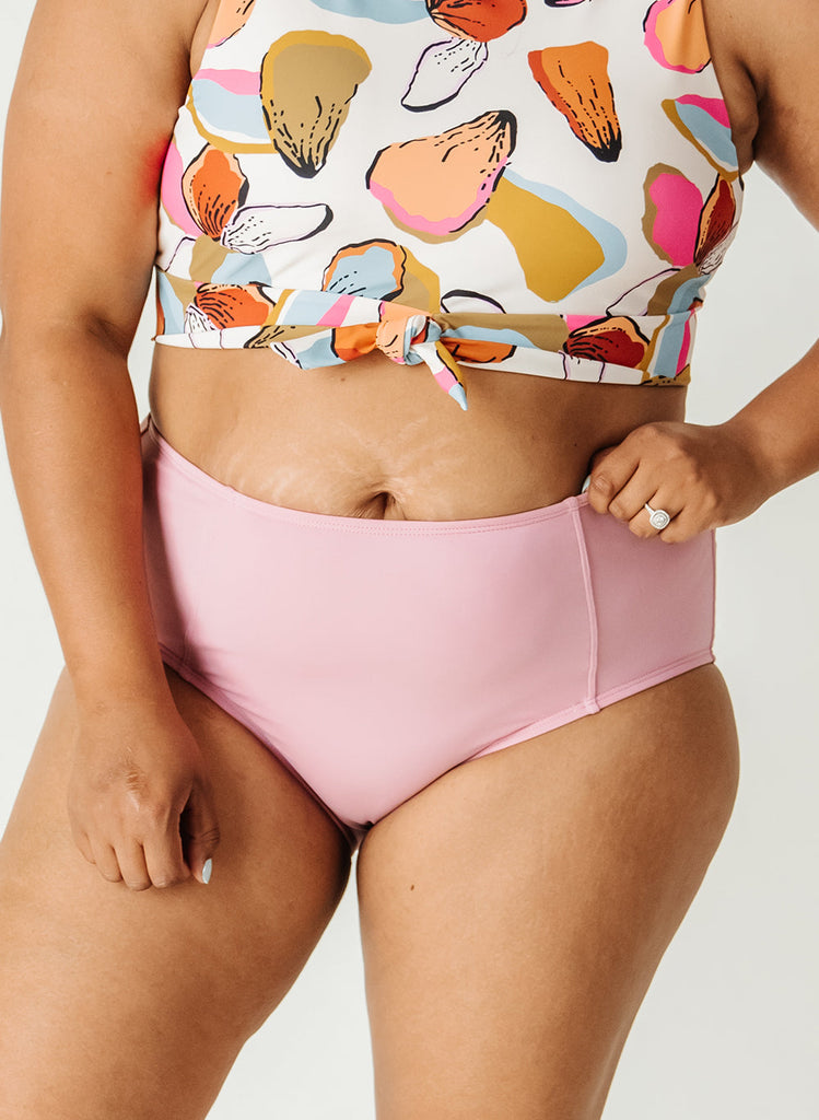 Photo of woman wearing a multi colored geometric pattern cropped swim top with light pink high waist swim bottoms