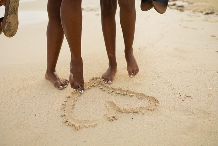 Mother and daughter drawing a heart in the sand with their feet.