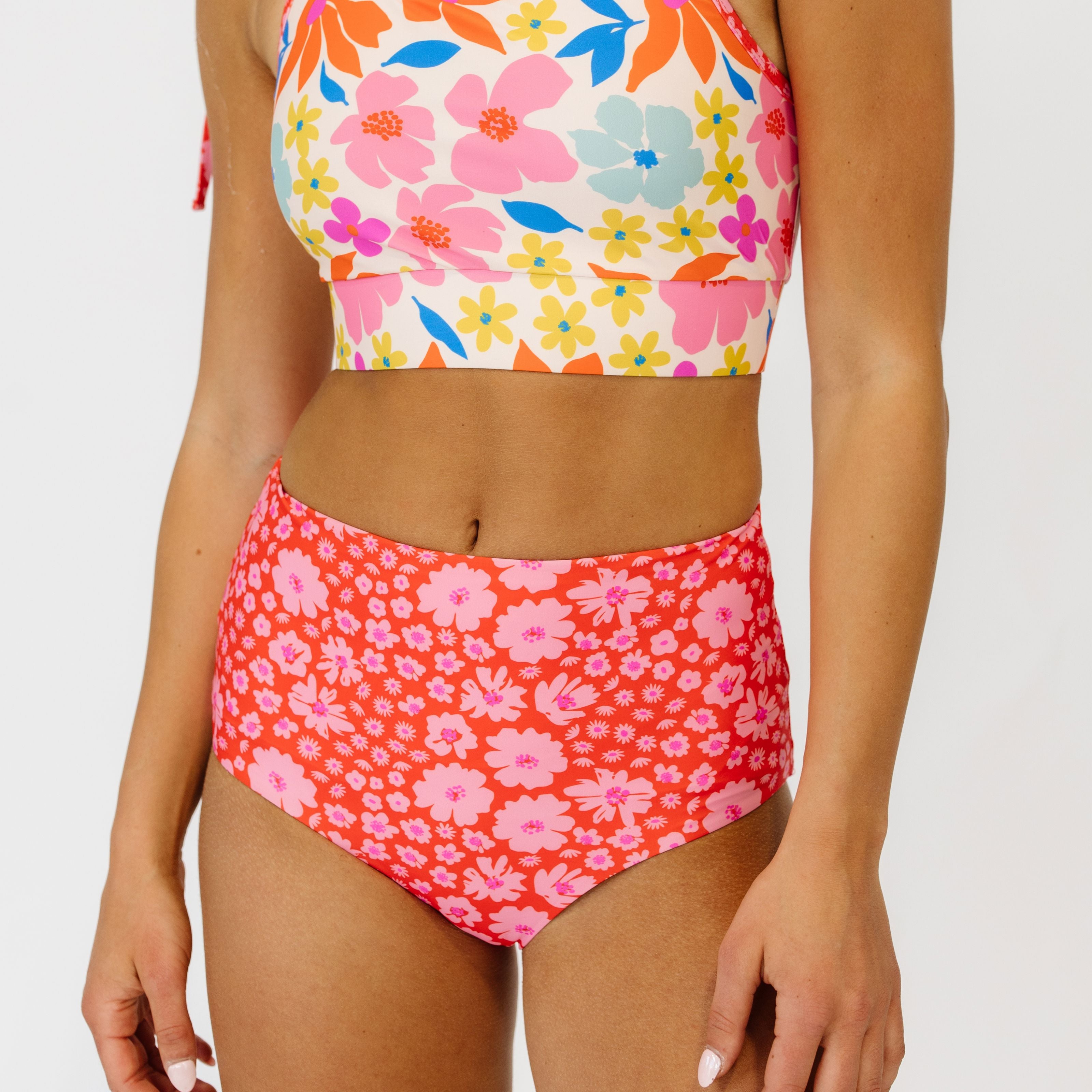 Close up image of a woman wearing a colorful, artsy floral tankini top and a pink and red scattered floral high-waist bottom