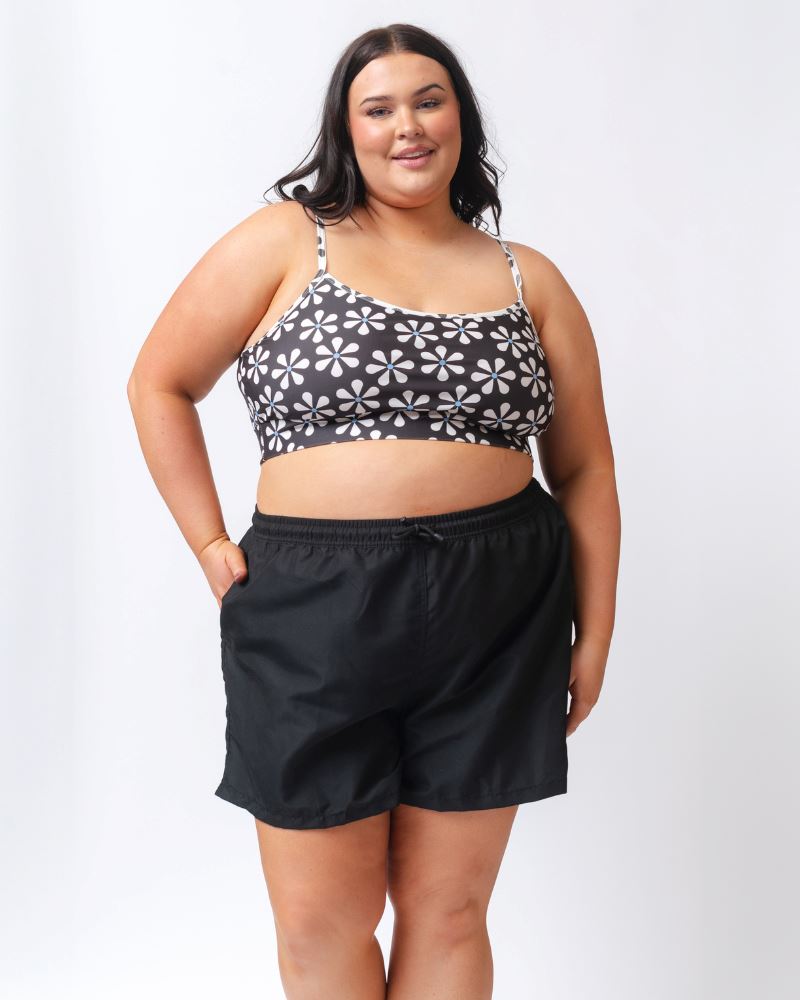 Photo of a woman wearing a black board short swim bottom and a black and white floral swim bralette