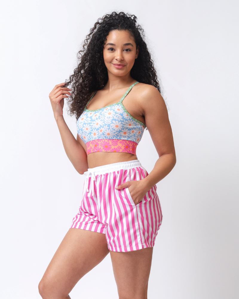 Photo of a woman wearing a pink and white striped board short swim bottom and a multi-colored floral swim bralette- side angle