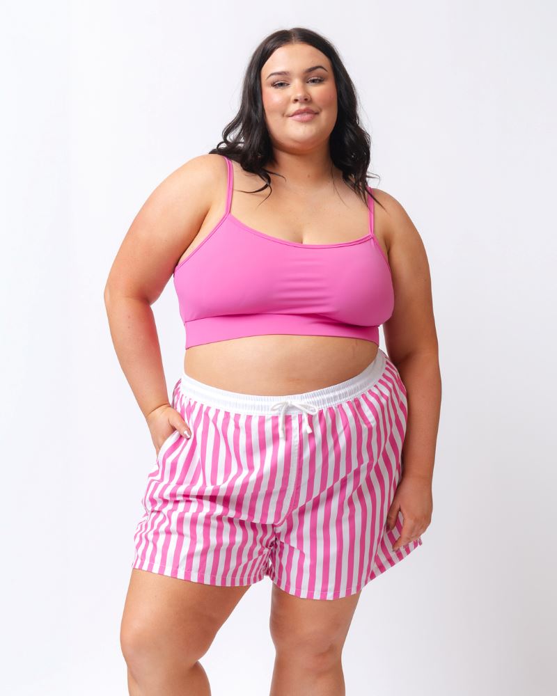Photo of a woman wearing a pink and white striped board short swim bottom and a dark pink swim bralette