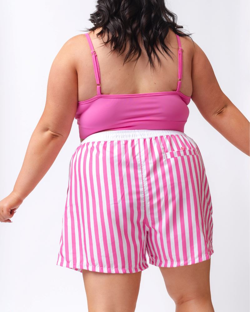Photo of a woman wearing a pink and white striped board short swim bottom and a dark pink swim bralette- back angle