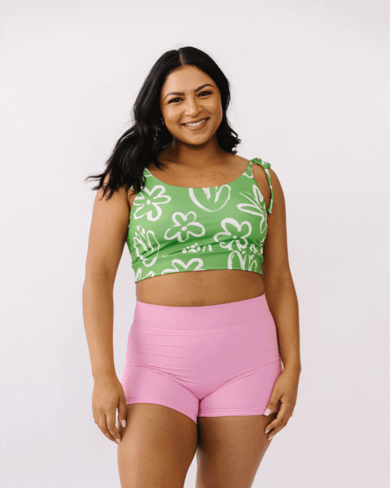 GIF of woman wearing green and white floral cropped swim top with pink boy short swim bottoms