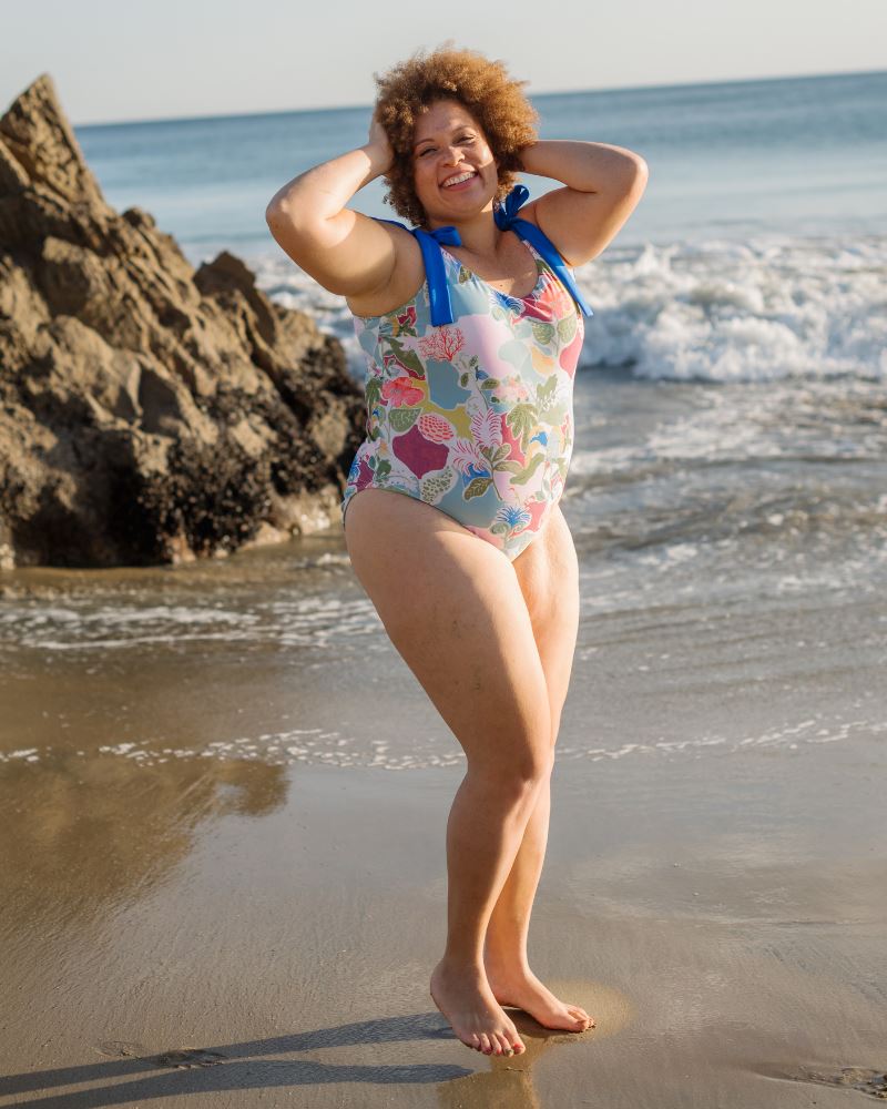 Photo of a woman posing on the beach wearing a colorful seashell inspired shoulder-tie one-piece swim suit